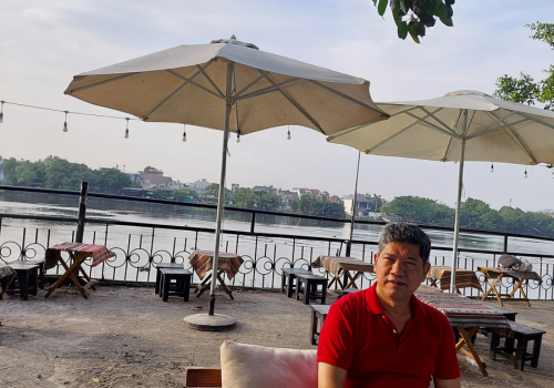 Mr. Khanh is sitting at a cafe near the river.